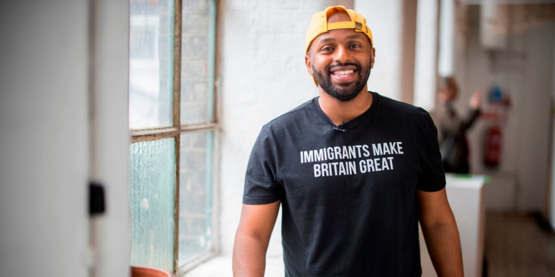 Magid Magid is smiling and wearing a black t shirt and a yellow cap